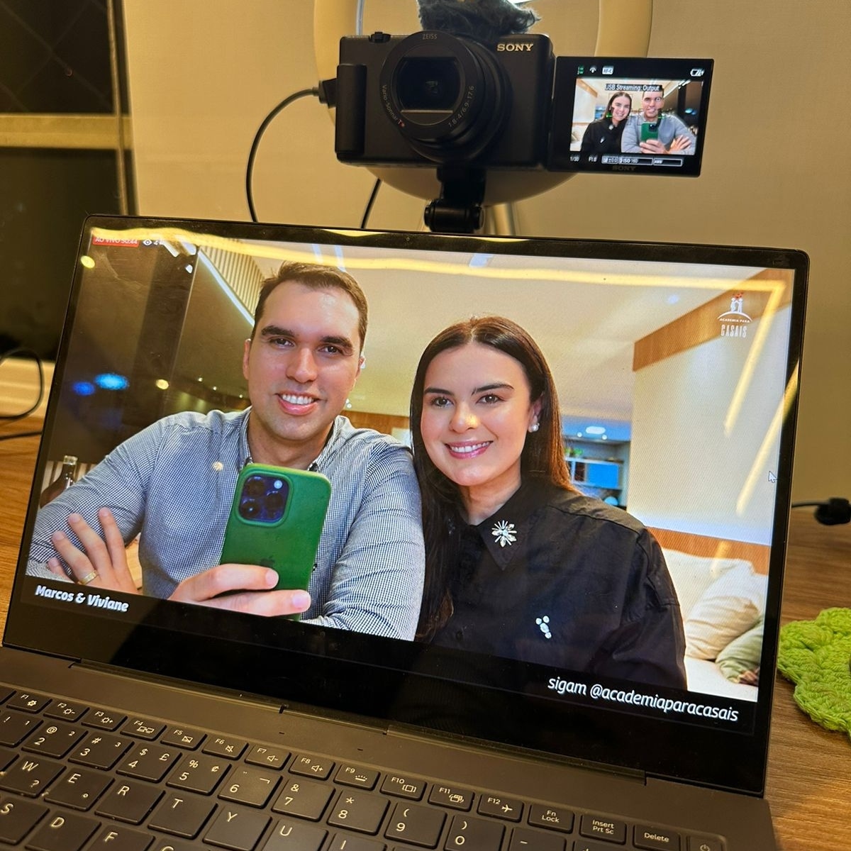 Marcos e Viviane na tela de um notebook, com uma câmera acima, durante uma conversa online